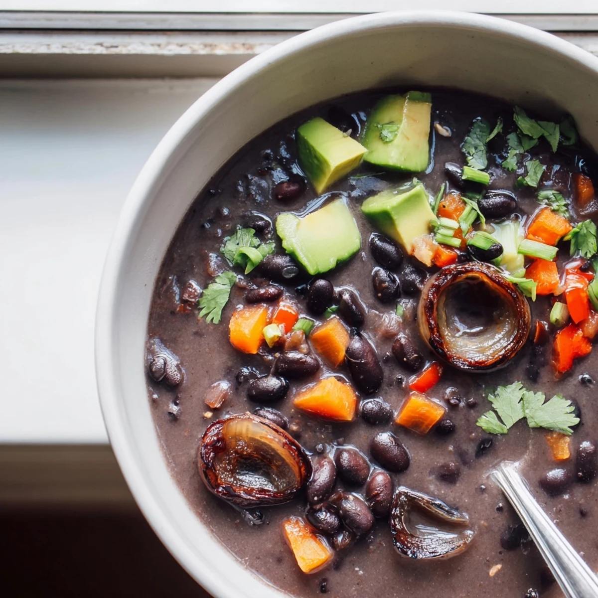 Steaming bowl of smoky black bean and roasted shallot hearty soup topped with fresh cilantro and avocado