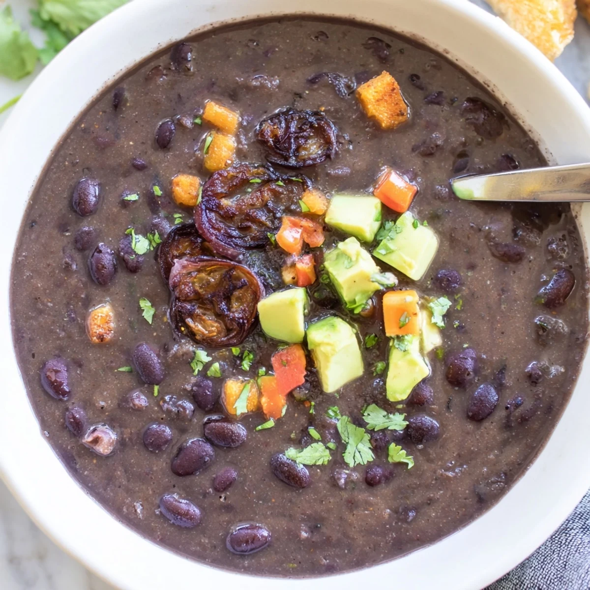 Smoky black bean and roasted shallot hearty soup garnished with lime wedges beside crusty bread