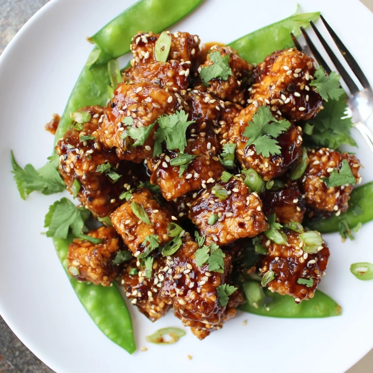Crunchy sesame snap peas topped with saucy crispy chili garlic tofu and fresh cilantro