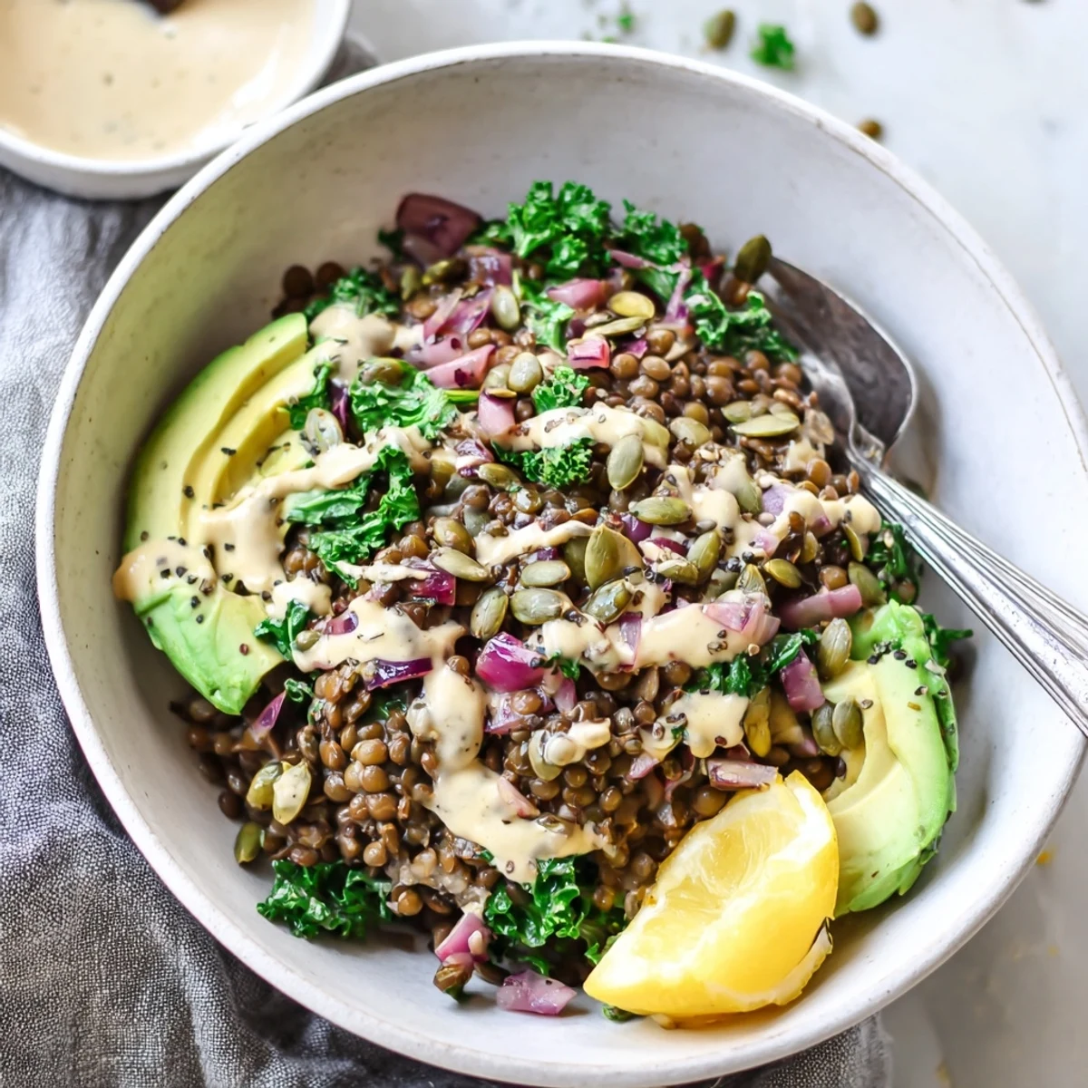 A vibrant savory lemon tahini lentil and spinach breakfast bowl drizzled with creamy sauce.