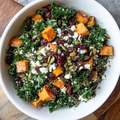 Forkful of the Seasonal Kale Bowl with toasted pumpkin seeds and tart dried cranberries over a wooden table.