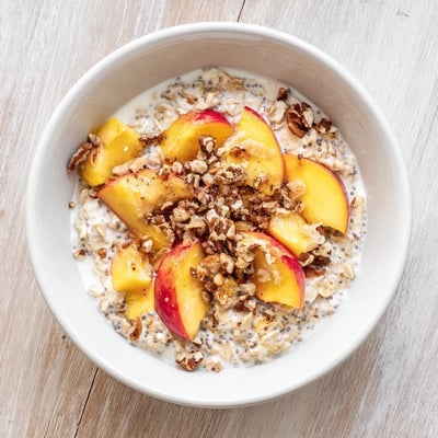 This Peach Cobbler Overnight Oats Breakfast Bowl features creamy oats layered with sweet peaches and crunchy pecans on top.