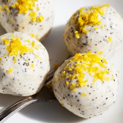 A hand reaching for a creamy Lemon Poppy Seed Cashew Bliss Sweet Treat bite next to a cup of herbal tea.