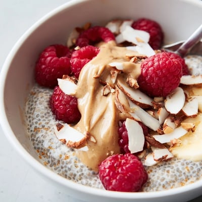 A wholesome Raspberry Almond Butter Chia Breakfast Bowl with sliced almonds and honey drizzle on a wooden table.  