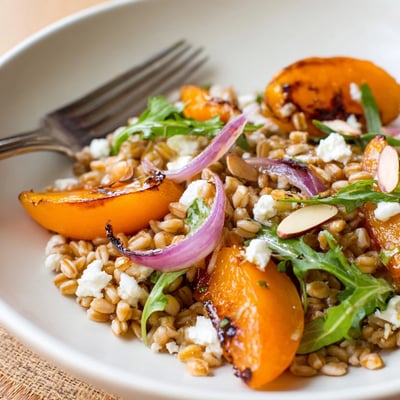 Bright Roasted Apricot Rosemary Farro Grain Salad topped with crumbled feta and arugula